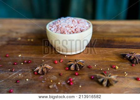 Pink Himalayan salt in a white bowl on wooden surface covered with anise and red peppercorn