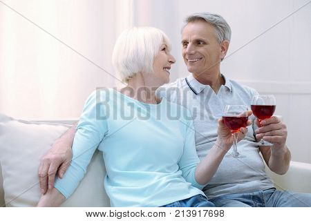 Wedding anniversary. Glad romantic joyful old couple drinking wine while celebrating their wedding anniversary