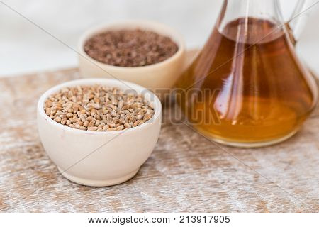 Close up wooden bowl with wheat grains and seed oil in decanter organic food concept
