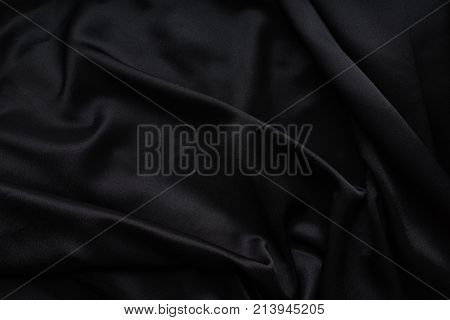 Dark black silky, satin fabric, wave, draperies. Beautiful textile backdrop to create creative layouts for black Friday. Close-up. Top view