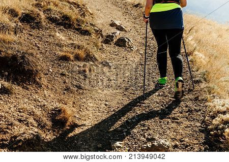 back woman walking on mountain trail with trekking poles
