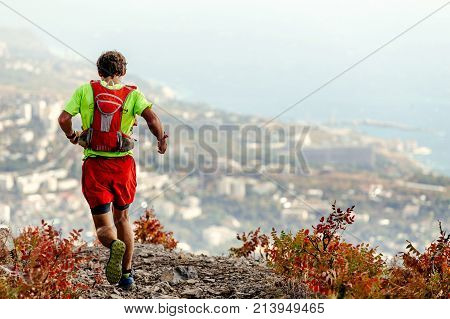 back male athlete running mountain trail background sea and urban