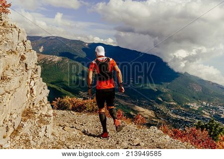 male runner running on mountain peak in background forest and clouds