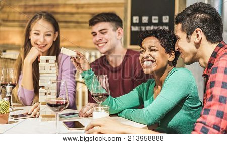 Young Students playing board game at hostel living room - Diverse culture people having fun and drinking wine at pub restaurant - Friendship and alternative evenings concept - Focus on afro girl face
