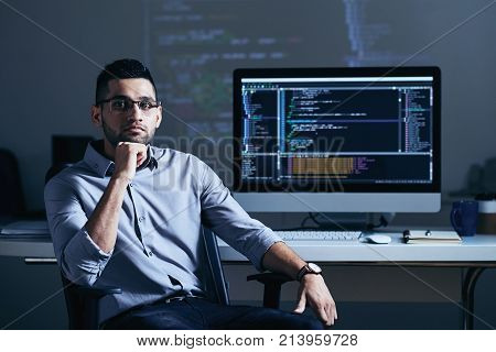 Indian professional programmer sitting at his table with big monitor