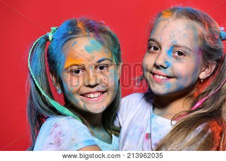 Girls with smiling face stand on red background close up. Creativity and education concept. Kids with ponytails stand close. Schoolgirls have paint spots on faces.