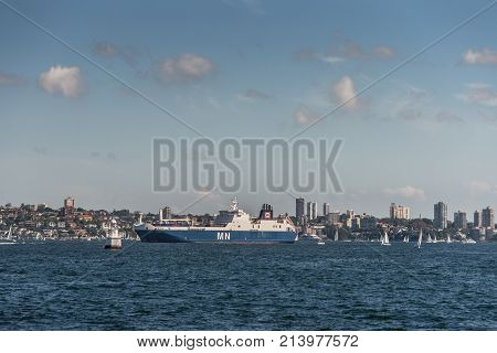 Sydney Australia - March 26 2017: Blue white French MN Calao RO-RO Cargo Ship in Sydney harbor on blue water under open sky with residential housing on shore in background.