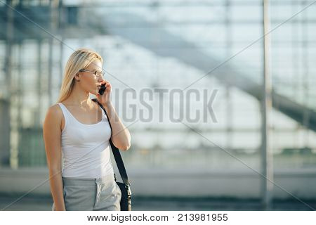 Attractive business woman using a phone and clock while standing in front of windows in an office building overlooking the city