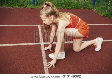 A full lenth portrait of a sporty teenager girl posing on the sports ground near the net. Sport fashion, active lifestyle, running.