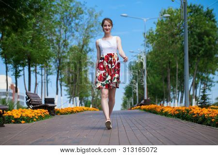 Full body portrait of a beautiful young brunette woman walking in flowers dress, summer park outdoors