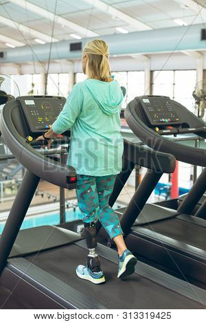 Rear view of disabled active senior Caucasian woman with leg amputee exercising on treadmill in fitness studio. Strong active senior female amputee training and working out