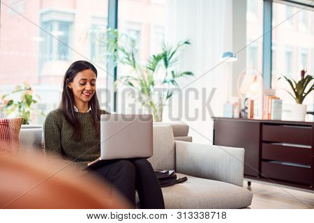 Businesswoman Sitting On Sofa Working On Laptop At Desk In Shared Workspace Office
