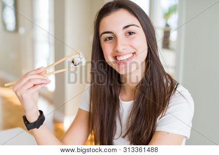 Beautiful young woman eating asian sushi using chopsticks with a happy face standing and smiling with a confident smile showing teeth