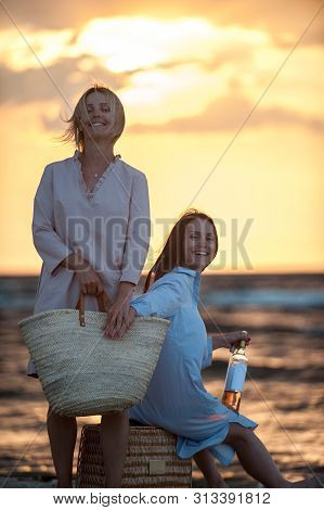 Two Young Women Having Fun Drinking White Wine Together On Seaside At Sunset. Friends/sisters. Summe