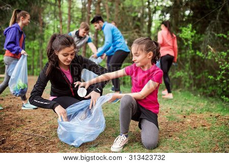 Group Of Active People Picking Up Litter In Nature, A Plogging Concept.