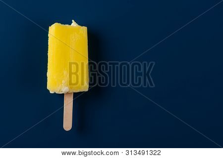 Yellow Popsicle With Some Bites On A Dark Blue Background