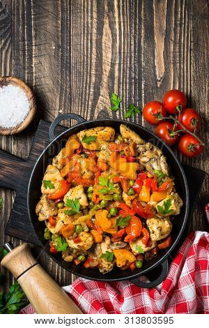 Chicken Stir Fry With Vegetables In The Black Iron Plate. Top View On Dark Wooden Background.