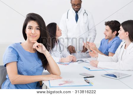 Meeting Of Medical Staff. Nurse Smiling To Camera At Meeting With Medical Team On Background