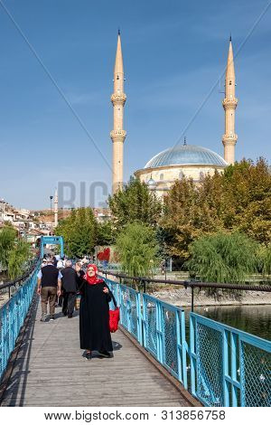Avanos, Turkey - October 19, 2018: Unidentified muslim woman making photo at the bridge over Kizilirmak River with Avanos mosque at background