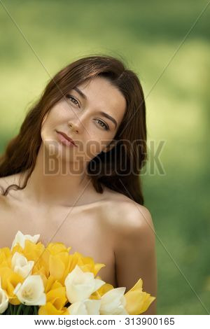 Attractive Woman In Red Dress With A Bouquet Of Spring Flowers Against Nature Bokeh Green Background