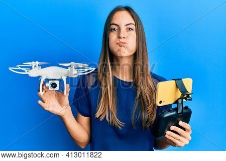Young beautiful woman taking a selfie photo with smartphone flying drone puffing cheeks with funny face. mouth inflated with air, catching air. 