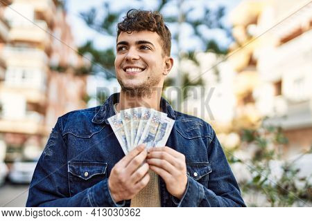 Young hispanic man smiling happy holding peruvian sol banknotes at the city