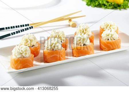 Philadelphia Sushi Roll made with Smoked Salmon. Maki sushi topped with cream cheese. White plate with wooden chopstick on white table
