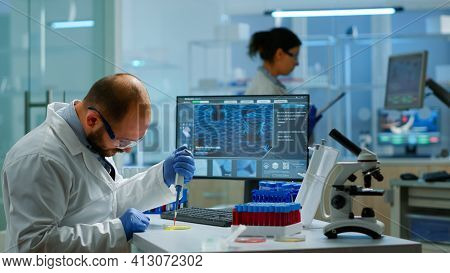 Man Scientist Using Micropipette For Filling Test Tubes In Modern Equipped Laboratory. Team Of Resea