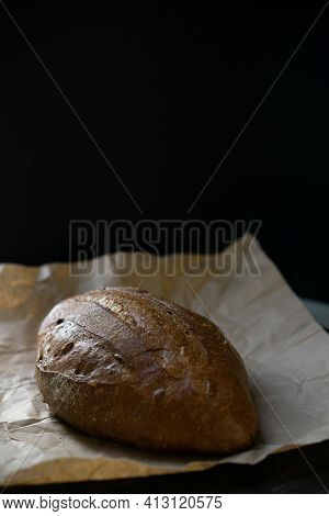 Whole Loaf Of Rye Or Wheat Dark Bread On Parchment Paper On Black Background. Hot Fresh Wholegrain P