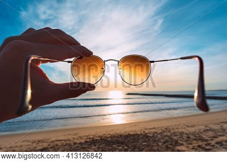 Hand Holding Stylish Round Sunglasses With Brown Lenses At Sunset. Putting On Sunglasses At Sunny Su