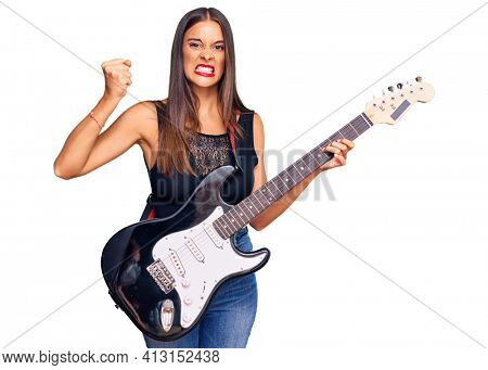 Young hispanic woman playing electric guitar annoyed and frustrated shouting with anger, yelling crazy with anger and hand raised 