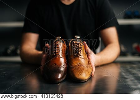 Close-up Hands Of Male Shoemaker Holds Old Light Brown Leather Shoe And Repaired Shiny Shoes After R