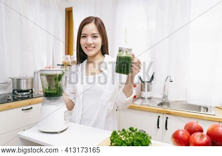 Portrait Of Beautiful Asian Woman Making Smoothie With Fresh Vegetables With Blender And Looking At 