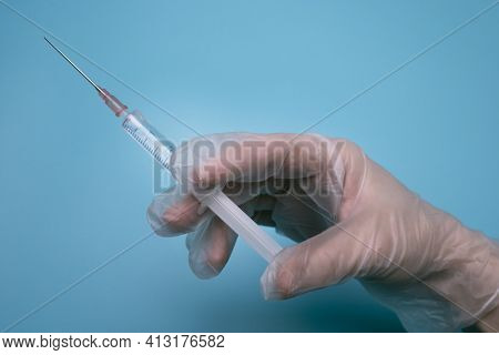Hand With A Syringe On The Blue Background.
