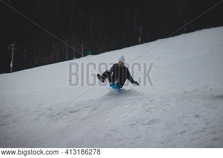 Boy From The Village In A White Cap Rode Down The Slope On A Plastic Snowboard To A Jumper And Jumps