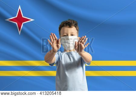 Little White Boy In A Protective Mask On The Background Of The Flag Of Aruba. Makes A Stop Sign With
