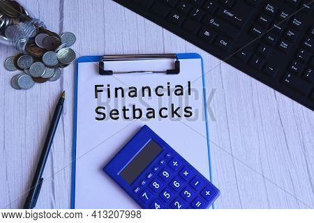 Text On Blue Clip Board With Calculator, Pen, Glass Jar With Coins And Keyboard - Financial Setbacks