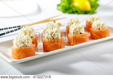 Philadelphia Sushi Roll made with Smoked Salmon. Maki sushi topped with cream cheese. White plate with wooden chopstick on white table