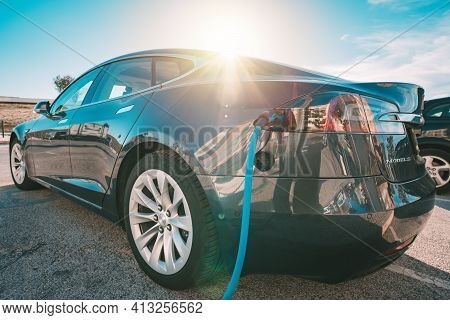 Charging Tesla Electric Car Or Ev Car On Parking Lot With Charging Station. Power Cable Supply Plugg