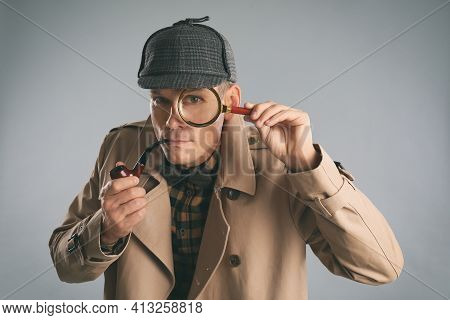 Male Detective With Magnifying Glass Smoking Pipe On Grey Background