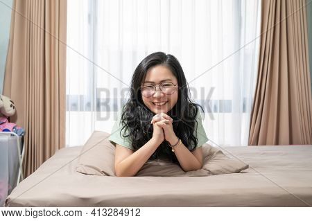 Beautiful Asian Woman Hold Her Hands Together While Lie On Her Stomach On Bed In Bedroom With A Past