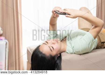 Beautiful Asian Woman Is Lying Down And Playing Mobile On The Bed In Her Bedroom With A Pastel Green