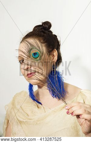 A Woman In Blue-feathers Earrings  And A Peackock Feather In Her Hand