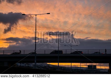 Spectacular Red Sunset With Dark Rainy Clouds Over The Bridge With Silhouettes Of People And Vehicle