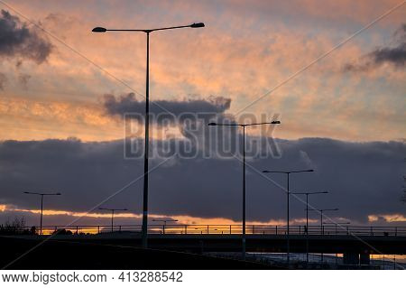 Spectacular Red Sunset With Dark Rainy Clouds Over The Bridge With Silhouettes Of People And Vehicle