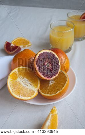 Sweet And Juicy Blood Oranges And Oranges, Whole And Cut On A White Plate And Gkasses Of Fresh Orang