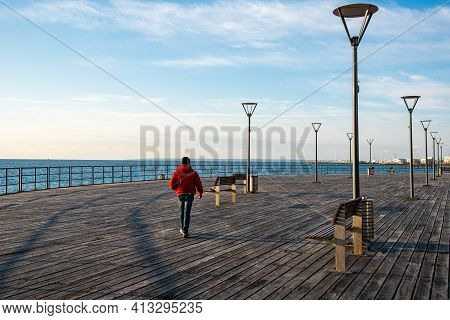 Unrecognized Person Dressed In Red Walking On Wooden Pier At Sea. Limassol Cyprus