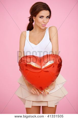 ผู้หญิงสวยงามน่าหลงใหลกับหัวใจสีแดงทรงบอลลูนวาเลนไทน์ pouting ริมฝีปากเธอประหนึ่ง blowi