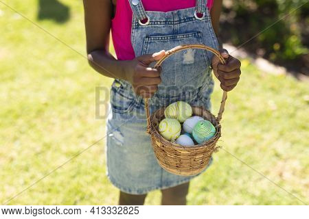 Midsection of african american girl holding basket while easter egg hunting. celebrating easter at home in isolation during quarantine lockdown.