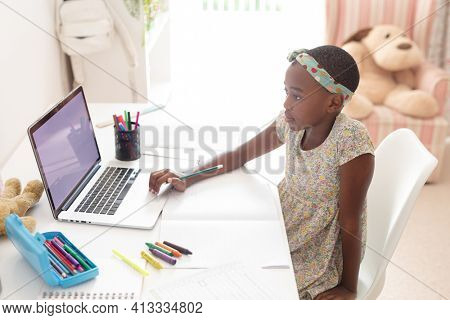 African american girl in bedroom at desk using laptop with copy space for online school lesson. staying at home in isolation during quarantine lockdown.